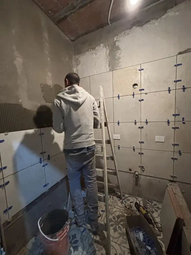 Albañil colocando porcelanato de gran formato en la pared de un baño, con crucetas niveladoras