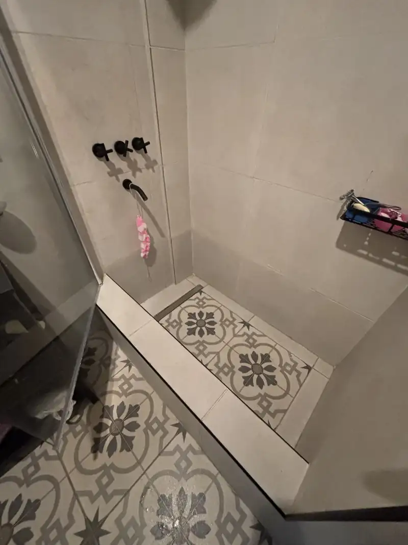 Ducha terminada con grifería negra, revestimiento cerámico y piso de mosaico calcáreo