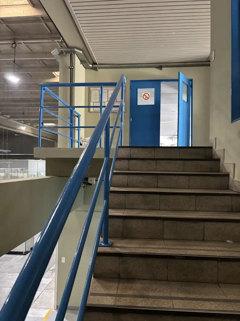 Escalera de una planta industrial con barandas pintadas de azul y paredes pintadas a nuevo