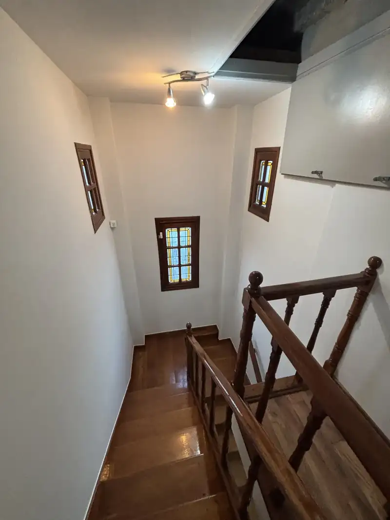 Escalera de madera con baranda torneada y paredes pintadas de blanco