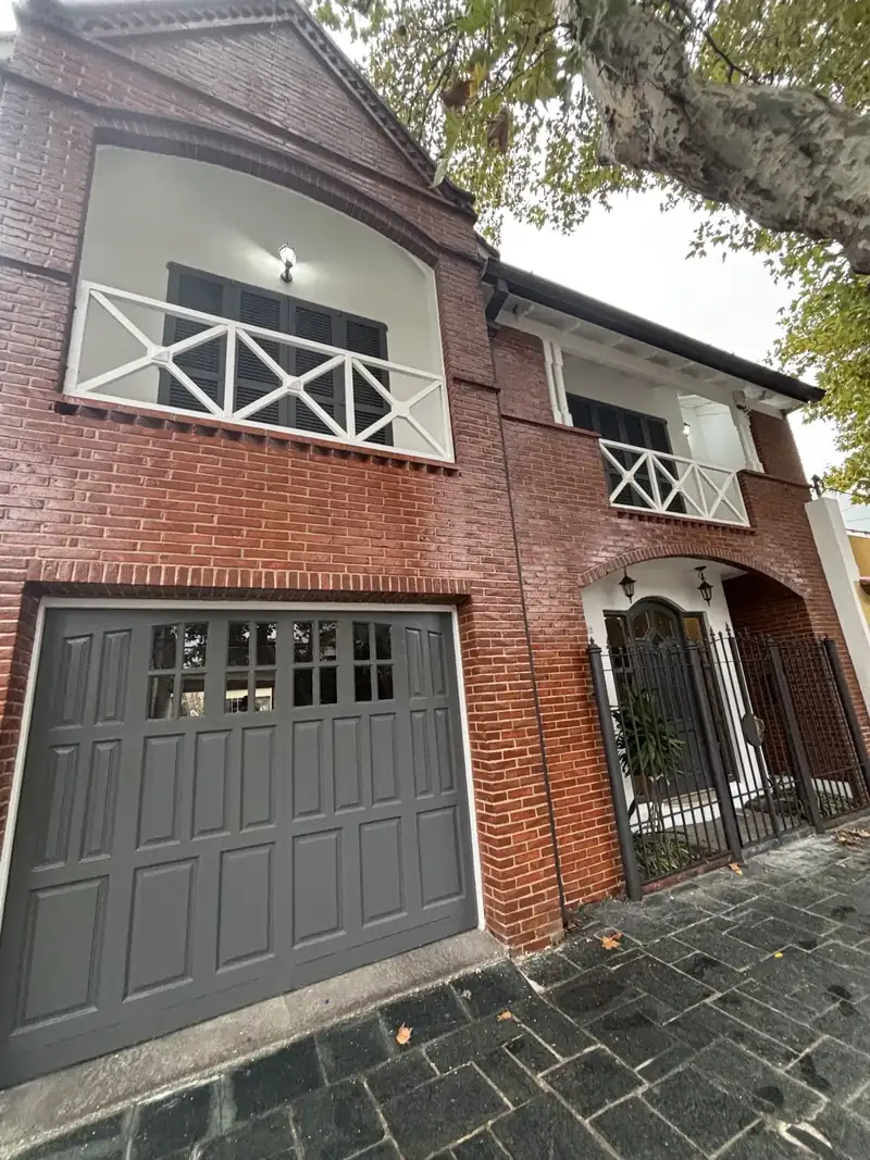 Frente de casa de ladrillo a la vista con balcón de baranda blanca y portón gris, recién pintado