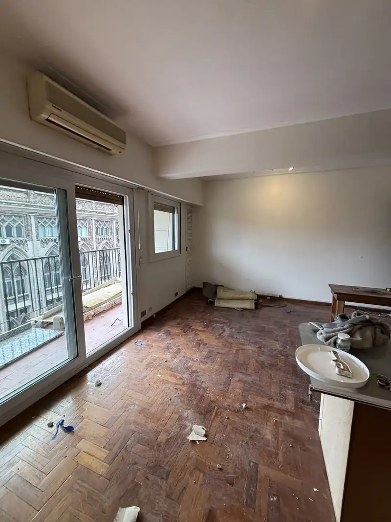 Living de departamento con piso de parquet y ventanal al balcón, durante la obra