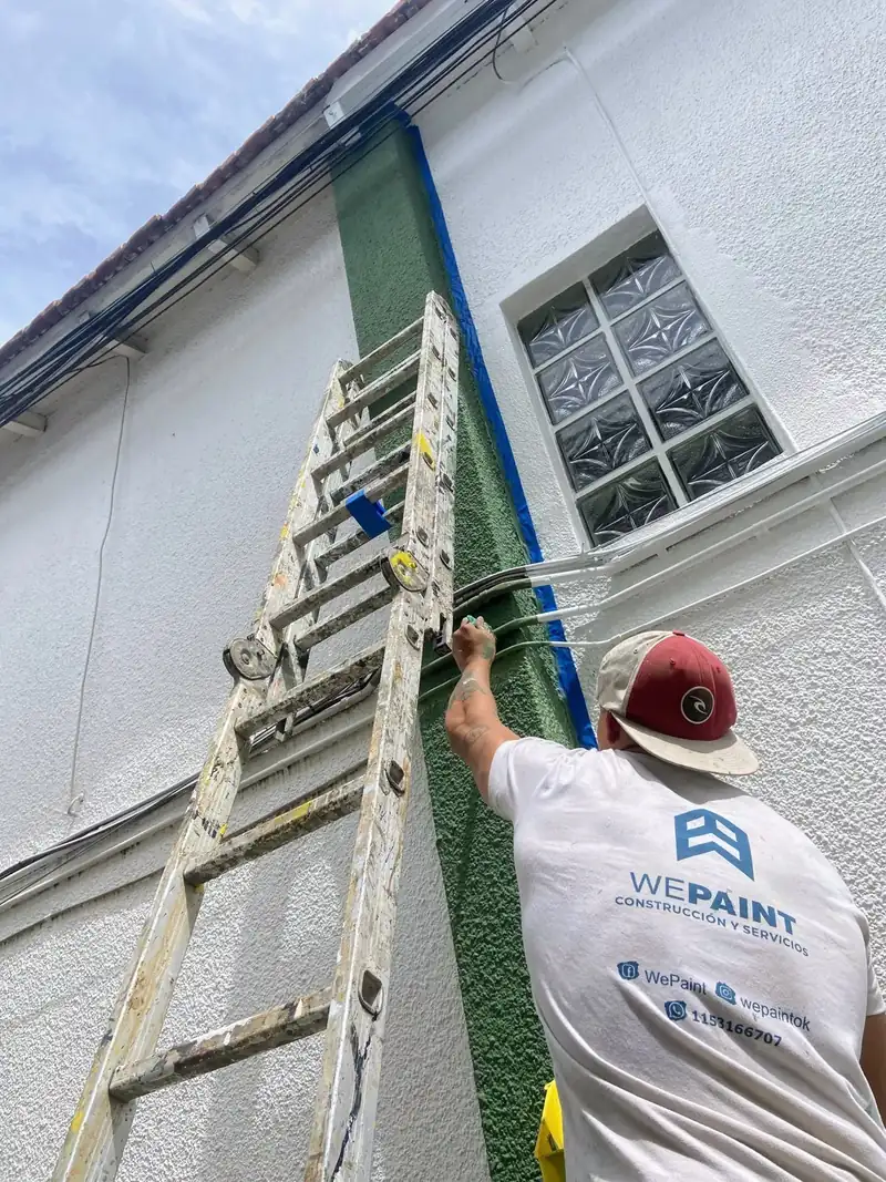 Pintor de WePaint con casco y remera de la empresa pintando la columna de una fachada desde una escalera